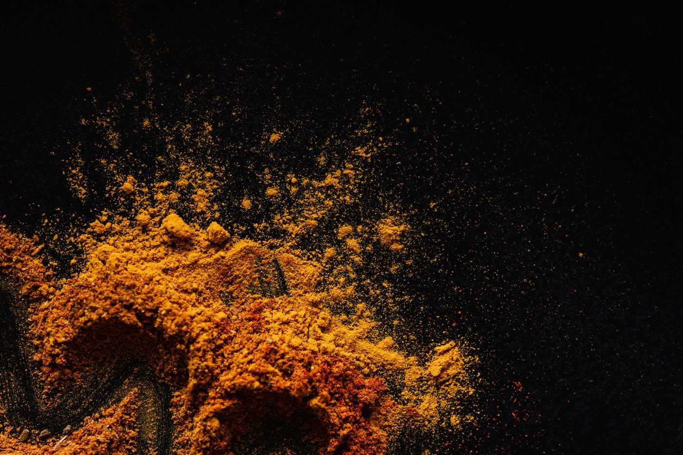 Golden turmeric powder bursting against a dark background